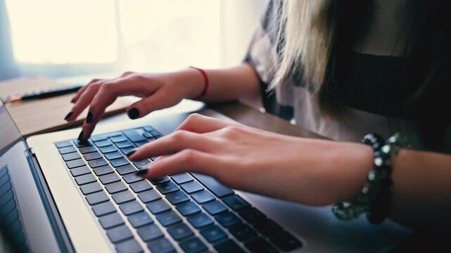 Close-up of female copywriter or student with black nail polish typing on laptop keyboard, work on remote project or studying online from home office.Digital workflow, remote job and modern lifestyle