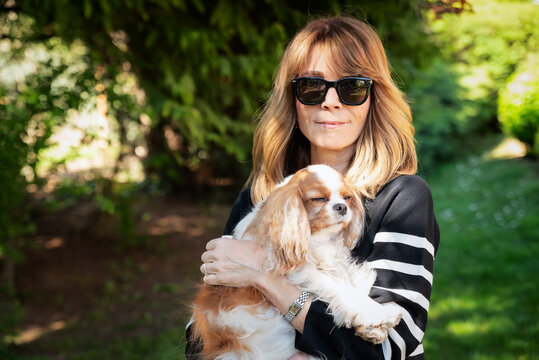 Portrait of a mature woman cudding a cute cavalier king chales spaniel dog in a garden