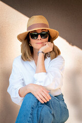 Fototapeta premium Portrait of a confident blond haired woman wearing sunhat and sunglasses outdoor