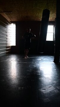 Cinematic Realism dramatic martial arts background dark gym, selective focus video of a man punching and kicking a kickboxing bag, blurred of focus background video.