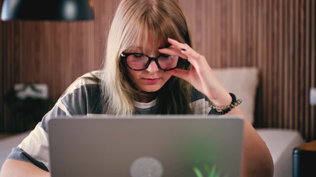 Overworked teenage girl feels eye strain and stress while studying on laptop at home. Experiencing computer vision syndrome from long hours of online learning, tired and overwhelmed screen time focus