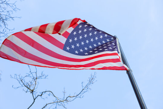 American flag waving in the wind against green trees and blue sky