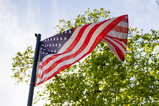 American flag waving in the wind against green trees and blue sky