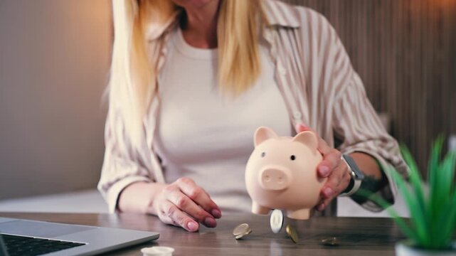 Woman shakes piggy bank trying to get remaining coins, symbolizing financial hardship and economic pressure. Concept of inflation, rising cost of living, savings depletion and financial struggle
