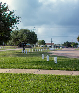 Small white post in the grass next to a parking lot lined with trees