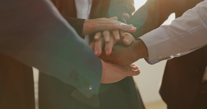 Closeup view of diverse business partners join hands as connectivity and unity symbol in office. Businesspeople express cooperation spirit in workplace