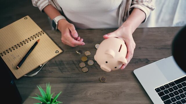 Top-down view of woman hands empty pink piggy bank and sorting euro coins on wooden desk. Financial reset concept, reviewing savings, organizing money flow and reassessing personal budget strategy