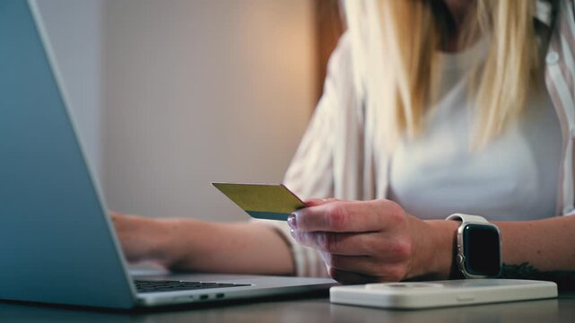 Young woman's hands holding a credit card and using a laptop for online shopping, confirming a purchase and entering payment information on an e-commerce website while sitting at home