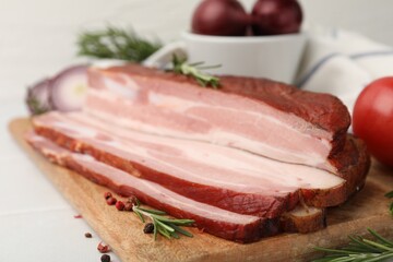 Fototapeta premium Pieces of smoked bacon with peppercorns and rosemary on light table, closeup