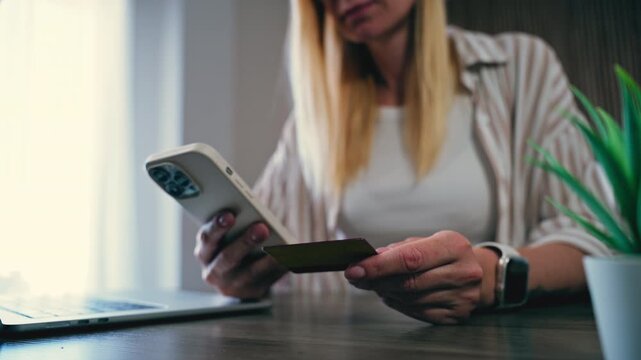 Female customer sitting at desk using smartphone and credit card for secure online transaction, enjoy convenience of digital banking and e-commerce from home office