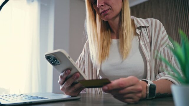 Blonde woman making secure online payment using smartphone and credit card while working from home. Focused freelancer confirming transaction on mobile app for e-commerce purchase