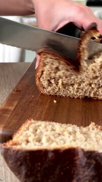 Close-up of a female hand cutting artisan sourdough bread on a wooden board. Fresh homemade loaf, rustic kitchen scene