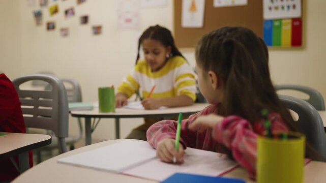 Little schoolgirl whispering to classmate during primary school classroom lesson