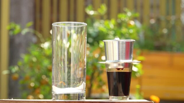 Pouring white sugar into a glass for Vietnamese coffee with phin filter in the background.