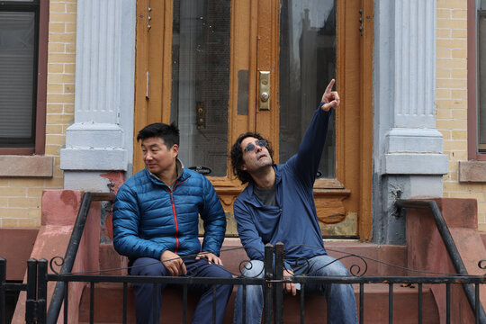 man pointing to something out of frame while sitting on urban brooklyn stoop nyc new york city life hanging out outside patio entrance to apartment building