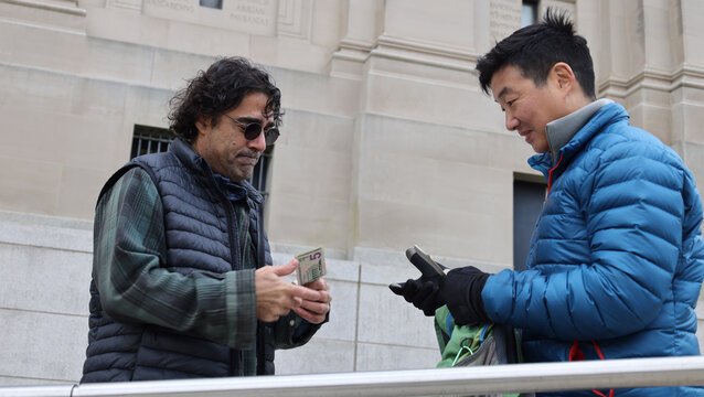 two men meet to buy sell a backpack for cash (transaction barter deal commerce selling buying) exchange purchase second hand person public used