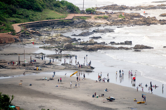High angle view of Sinquerim Candolim beach in Goa with people enjoying shoreline, rocky coast, and waves during a busy day.