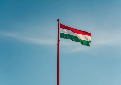 The national flag of hungary waving against a clear blue sky, representing hungarian patriotism and national identity in a bright outdoor setting