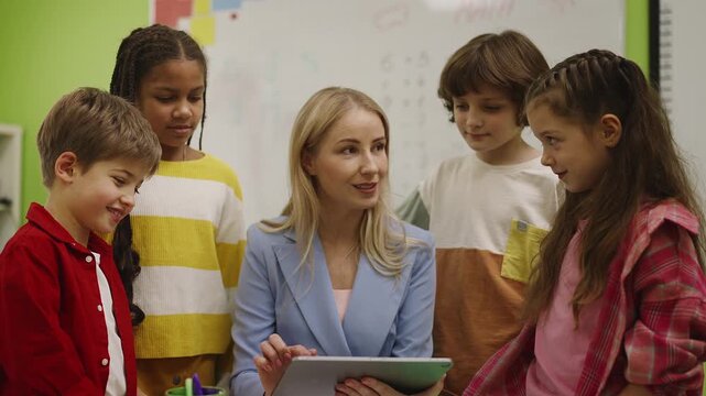 Friendly teacher helping pupils with project using tablet, classroom learning