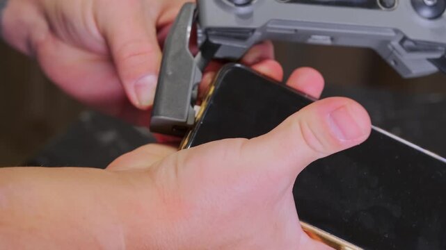 Close-up of hands connecting smartphone to drone remote control via cable, preparing device for flight operation, mobile interface setup, aerial technology workflow, modern gadget interaction
