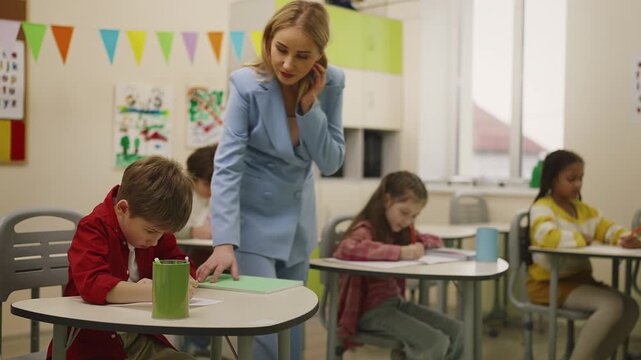Female teacher helping students during classroom test, primary education scene