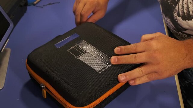 Close-up of male hands unzipping protective case and opening portable smoke machine, preparing equipment for macro photo and video shooting with atmospheric fog effects in studio setup