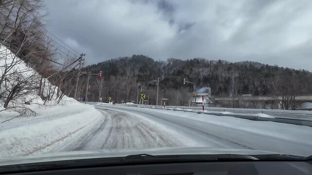 POV driving on a snowy winding mountain road with curve warning signs in Furano Hokkaido Japan winter landscape