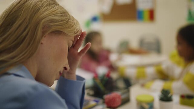 Stressed teacher holding head while pupils playing paper planes in classroom