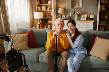 Obraz premium A home health nurse smiles as she sits next to an elderly man in a living room. They are enjoying each other's company while the nurse offers support.