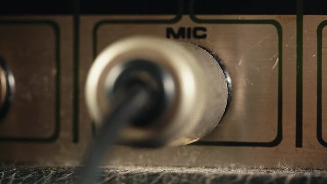 Close-up of plugging a jack into a bass guitar amplifier and turning up the volume knob, live concert show, playing music on guitar tube amplifier.