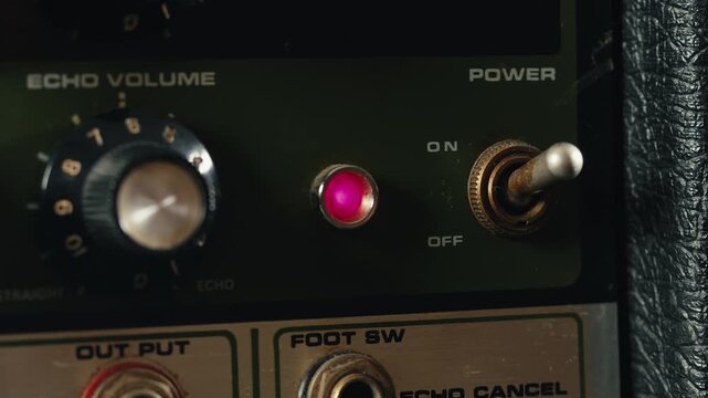 Close-up of plugging a jack into a bass guitar amplifier and turning up the volume knob, live concert show, playing music on guitar tube amplifier.
