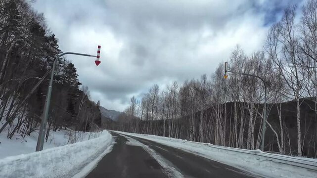 POV dashcam driving on a slippery slushy road in Furano Hokkaido Japan during winter with mountain forest view
