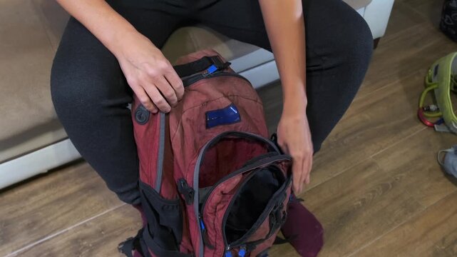 Woman closing a backpack at home while preparing for a trip, organizing personal items and finishing packing routine before travel or hiking adventure. Travel preparation at home