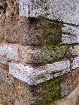 Sharp corner angle of a solid masonry building showing heavy stone blocks coated in thick organic green moss