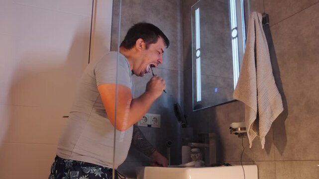 Middle aged white man brushes tongue with toothbrush at sink, maintaining oral hygiene and removing bacteria. Daily dental care routine, fresh breath concept and personal hygiene in bathroom at home