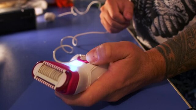 Close-up of male hands turning on epilator and shaving arm hair, testing different modes of electric hair removal device, personal grooming routine at home, hygiene and body care process