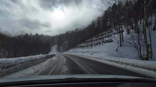 POV dashcam driving on a snowy mountain road in Furano, Hokkaido, Japan. Winter landscape with snow-covered trees and dramatic cloudy sky