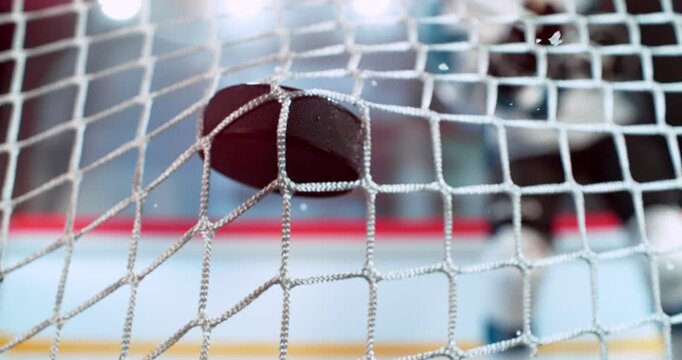 Extreme super slow motion close-up of a hockey puck hitting the goal net as a player scores, captured at 1000 fps, with ice particles and a blurred hockey player on the rink in the background.