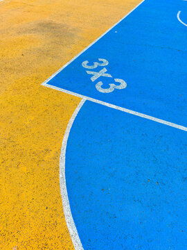 Street basketball court showing a three-on-three play area with vibrant blue and orange surfaces marked clearly for players in a friendly neighborhood setting