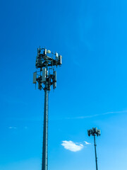 Obraz premium Two cell towers stand tall against a clear blue sky in a rural area during the afternoon light