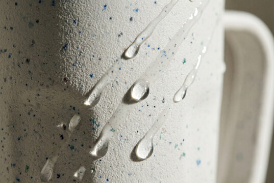Macro view of a speckled bio-plastic surface with crystalline water droplets. The shot highlights the unique grain of recycled composites and the physics of surface tension.
