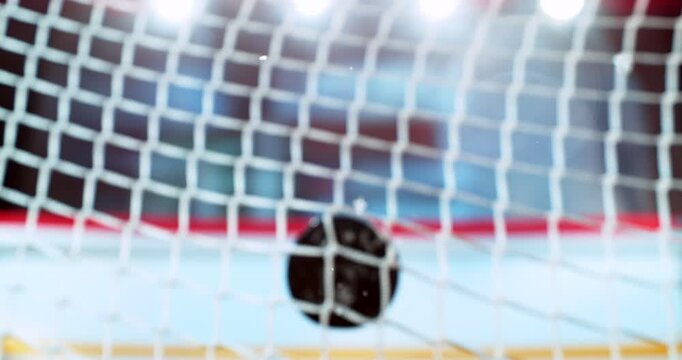 Extreme super slow motion close-up of an ice hockey puck striking the goal net at 1000 fps, with ice particles exploding on impact and a blurred winter stadium and rink in the background. Speed ramp.
