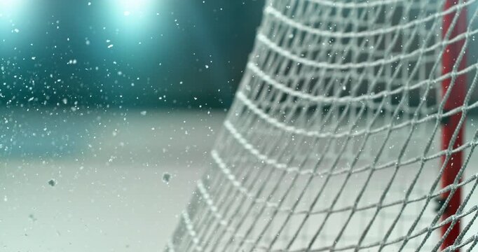 Extreme super slow motion close-up of an ice hockey puck striking the goal net at 1000 fps, with ice particles exploding on impact and a blurred winter stadium and rink in the background. Speed ramp.