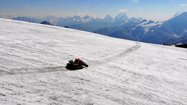 A snowcat in the snowy mountains moves towards the peaks. Snow-covered landscape with mountain peaks