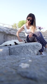 Woman petting stray cat on ancient theater stone benches in Teos, Turkey