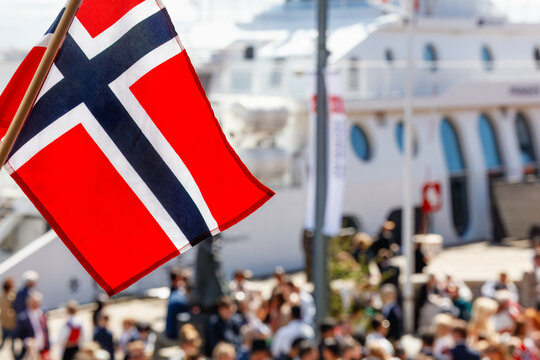 National identity and festive atmosphere: Norwegian flag waving above crowds celebrating Constitution Day at Aker Brygge waterfront in Oslo.