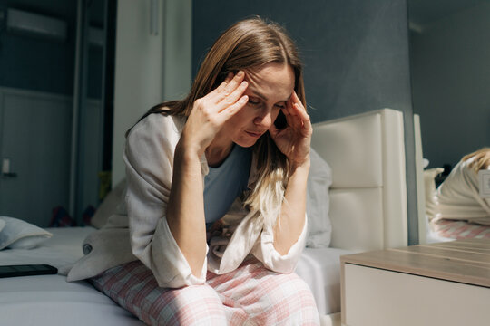 A middle-aged woman sitting at home holds her hands on her temples. Headache, women's health, hormonal levels. Financial crisis.