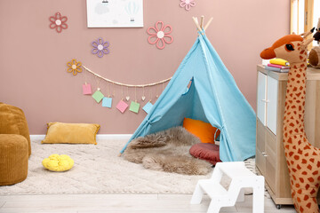 Colorful paper notes and beautiful decor hanging on beige wall near toy wigwam in stylish children's room with chest of drawers and poufs. Interior design © New Africa