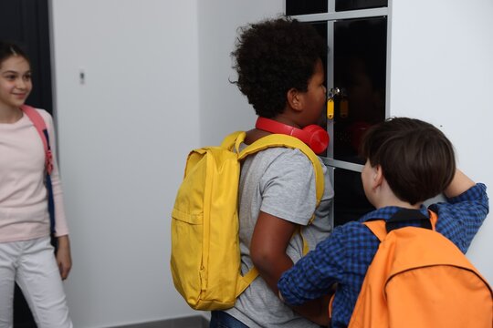 Boy bullying his African American classmate near lockers in school hallway