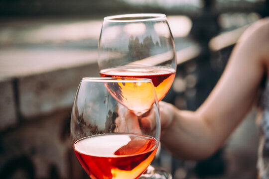 Hand holding glasses of rose wine in summer sunshine during a outdoors party or a picnic.